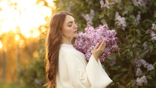 A woman smelling lilacs close to her face at sunset