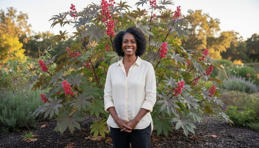 An African woman is standing in front of a castor bush smiling